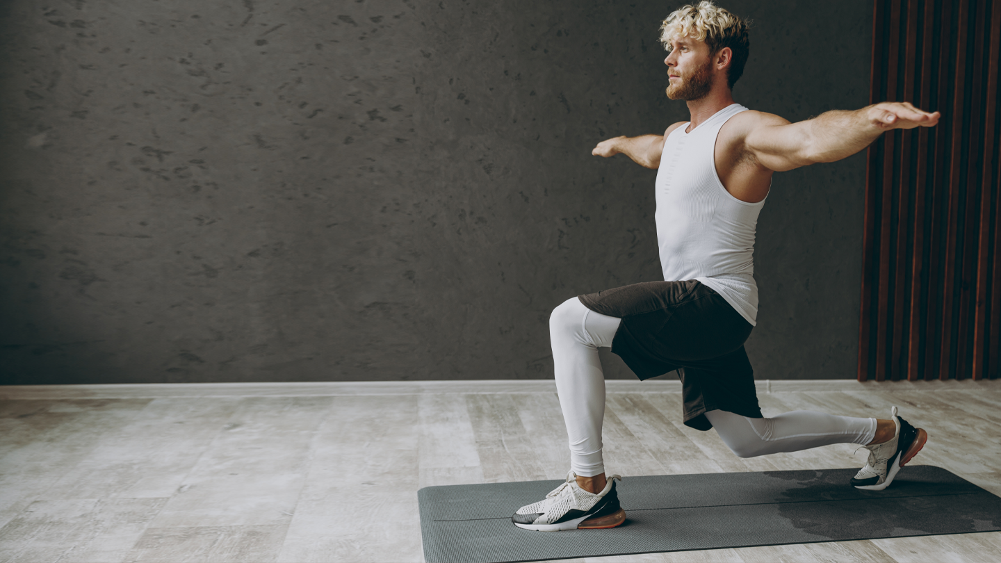 Muskulöser Mann führt Ausfallschritt auf Yogamatte in modernem Studio aus