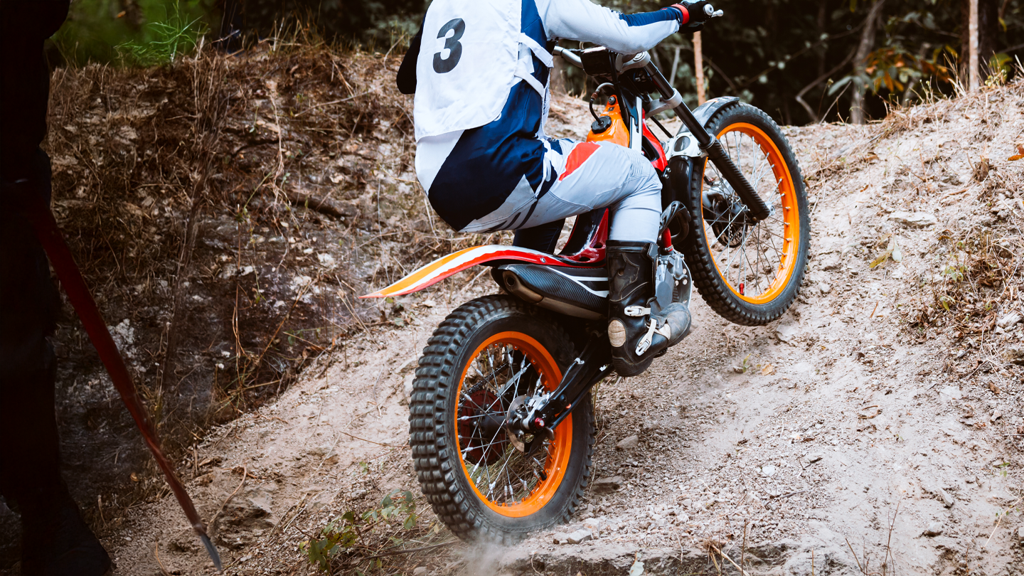 Trials motorcycle rider number 3 navigating steep dirt terrain on bike with orange rims