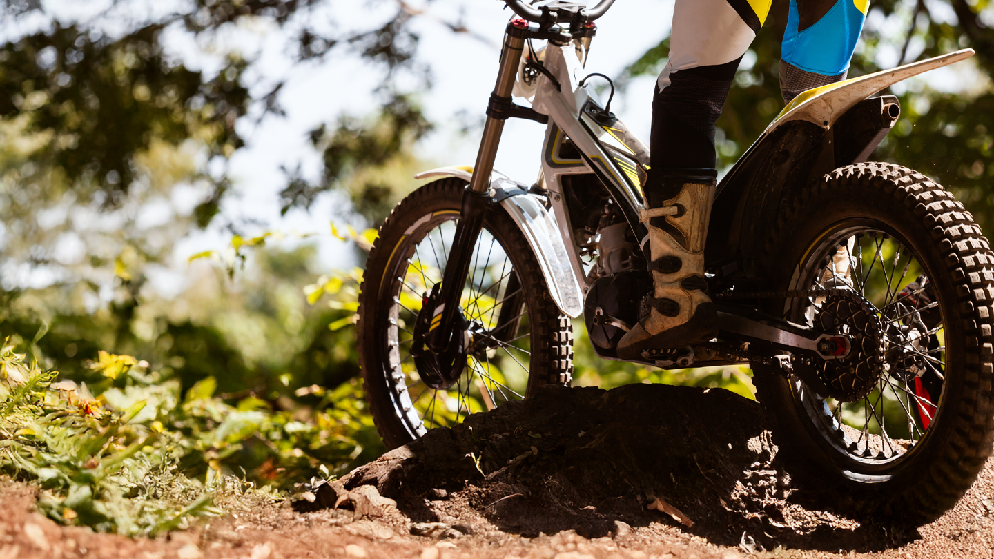 Close-up of trials motorcycle navigating rocky dirt terrain in forest setting with rider in protective gear