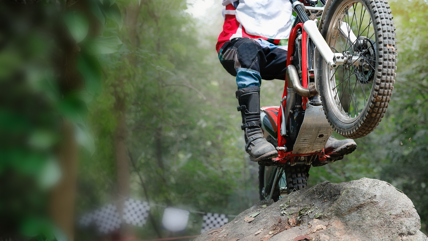 Trials motorcycle rider balancing on a large rock obstacle in a forest competition course