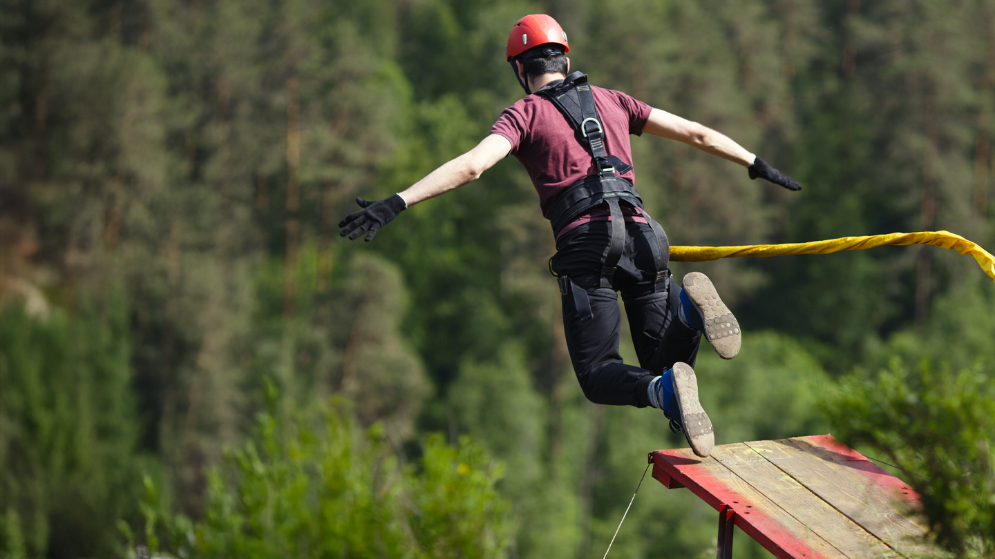 Person in safety harness and helmet leaping from a bungee jump platform
