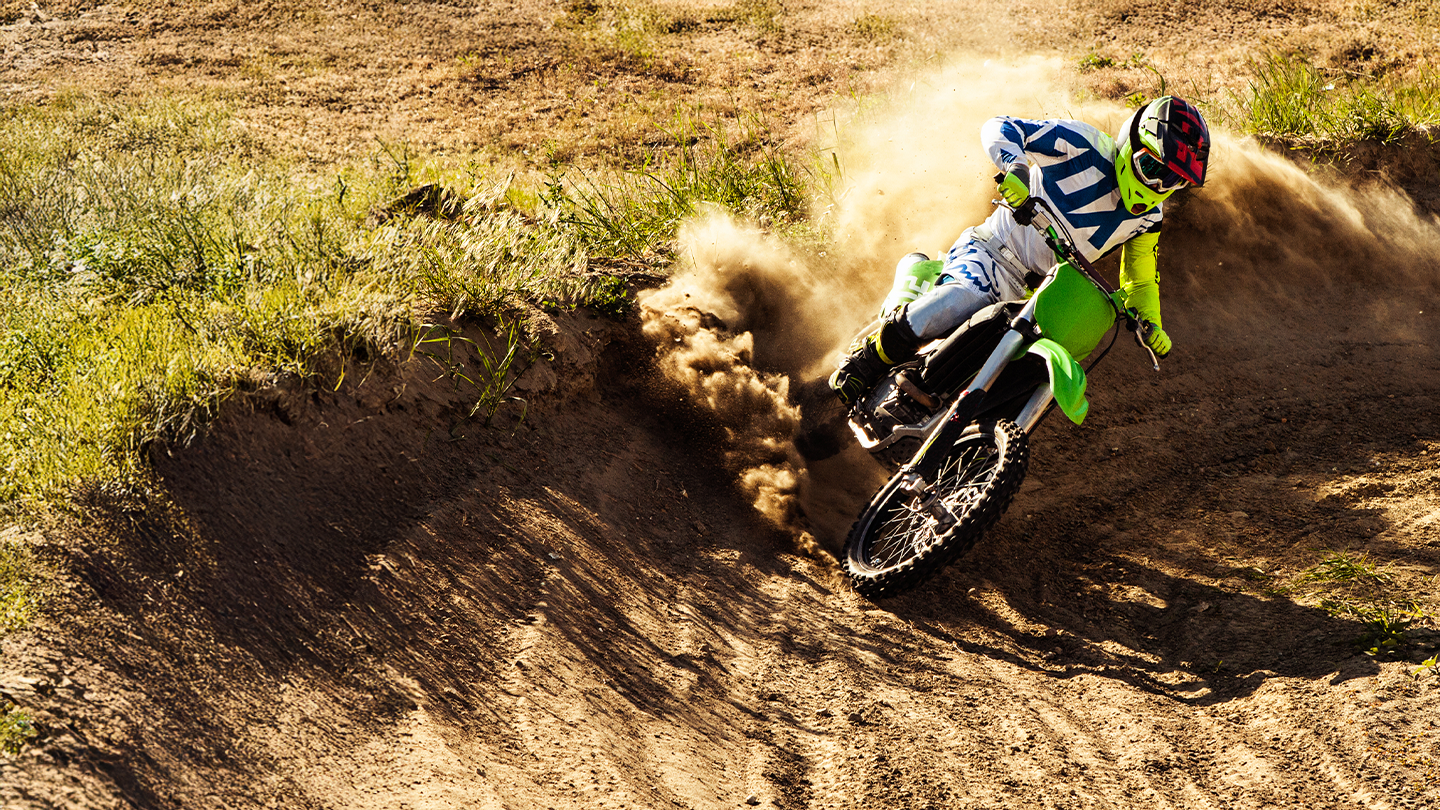 Motocross rider leaning into a sharp dirt track corner with a cloud of dust.